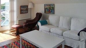 A living room with a white sofa, a brown leather chair, a white coffee table, and a colorful patterned rug.