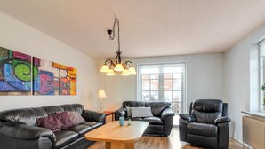 A living room with a black leather sofa, two armchairs, a wooden coffee table, and abstract art on the wall.