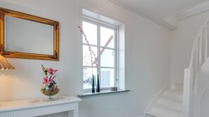 A room with a white console table, a mirror, a vase with flowers, a window with a view of a snowy landscape, and a wooden staircase.