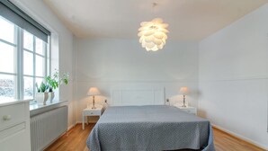 A bedroom with a bed, two bedside tables, a window with plants, and a unique ceiling light.