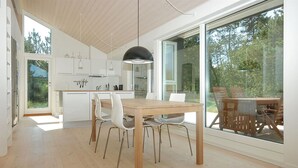 Een moderne keuken met witte kastjes, een houten eettafel en stoelen. Een groot raam biedt uitzicht op het omliggende landschap.
