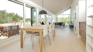 Een ruime kamer met een grote houten tafel en stoelen, een boekenkast en uitzicht op het groen.