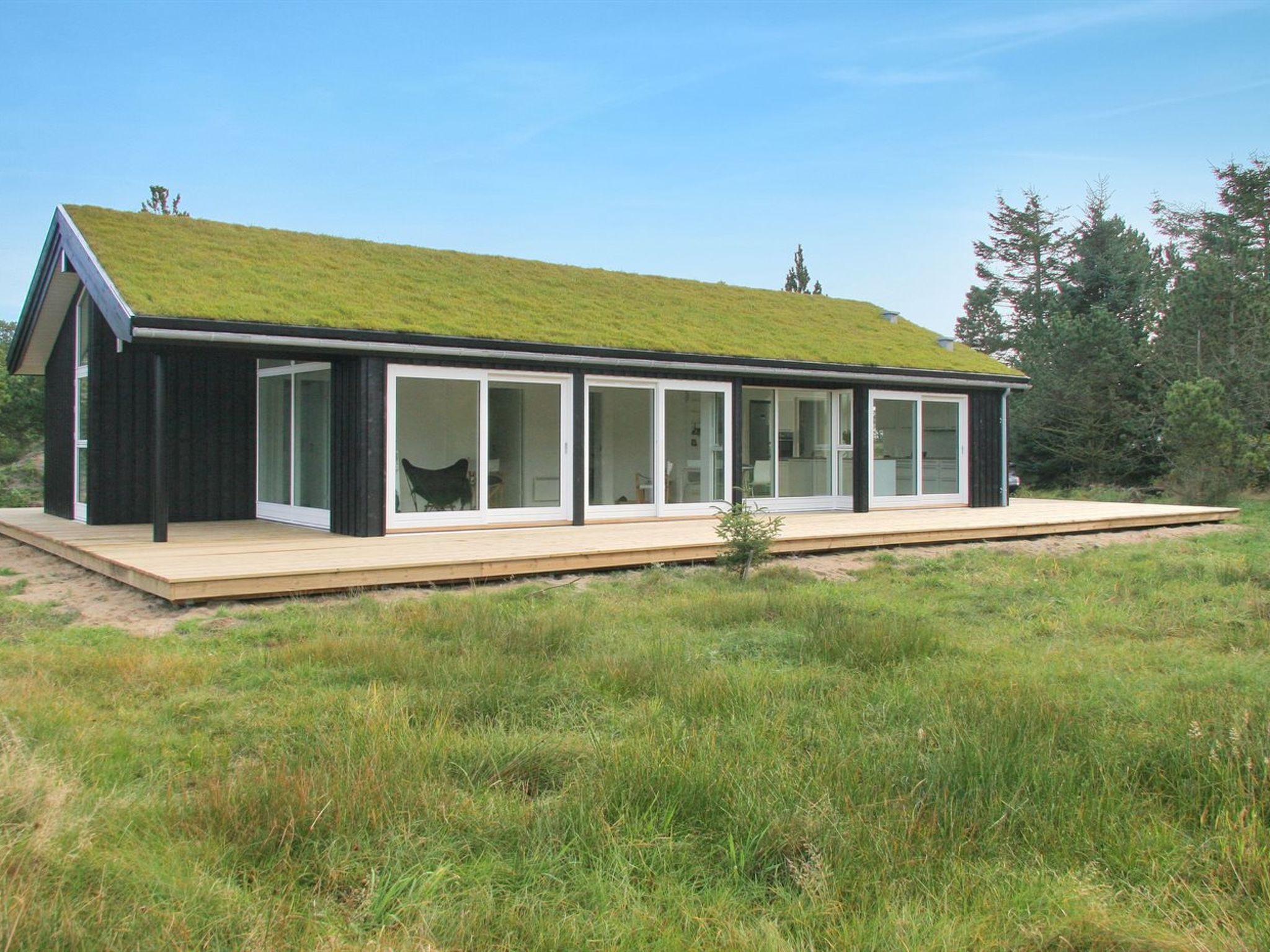 A modern house with a grass-covered roof, large sliding glass doors, and a wooden deck.