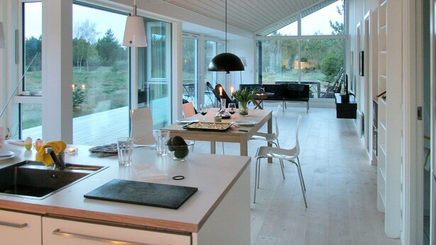 Een moderne keuken met een groot kookeiland, een eethoek met tafel en stoelen, en uitzicht op het groen.