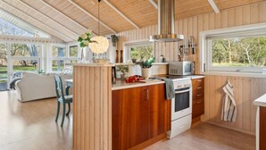 A modern kitchen with wooden cabinets, a built-in oven, and a microwave. There is a large window providing a view of the outdoors. - "Amola" - 1.6km from the sea by Interhome (Højby)