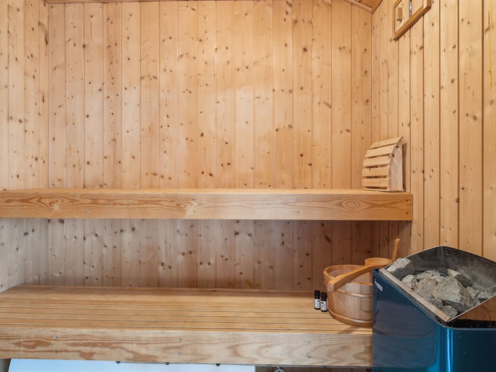 Uma sauna de madeira com dois bancos, um balde de madeira e um recipiente azul com pedras.