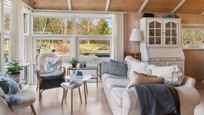 A cozy living room with a wooden ceiling, large windows offering a view of the outdoors, a white cabinet with glass doors, and a comfortable sofa with cushions. - "Amola" - 1.6km from the sea by Interhome (Højby)