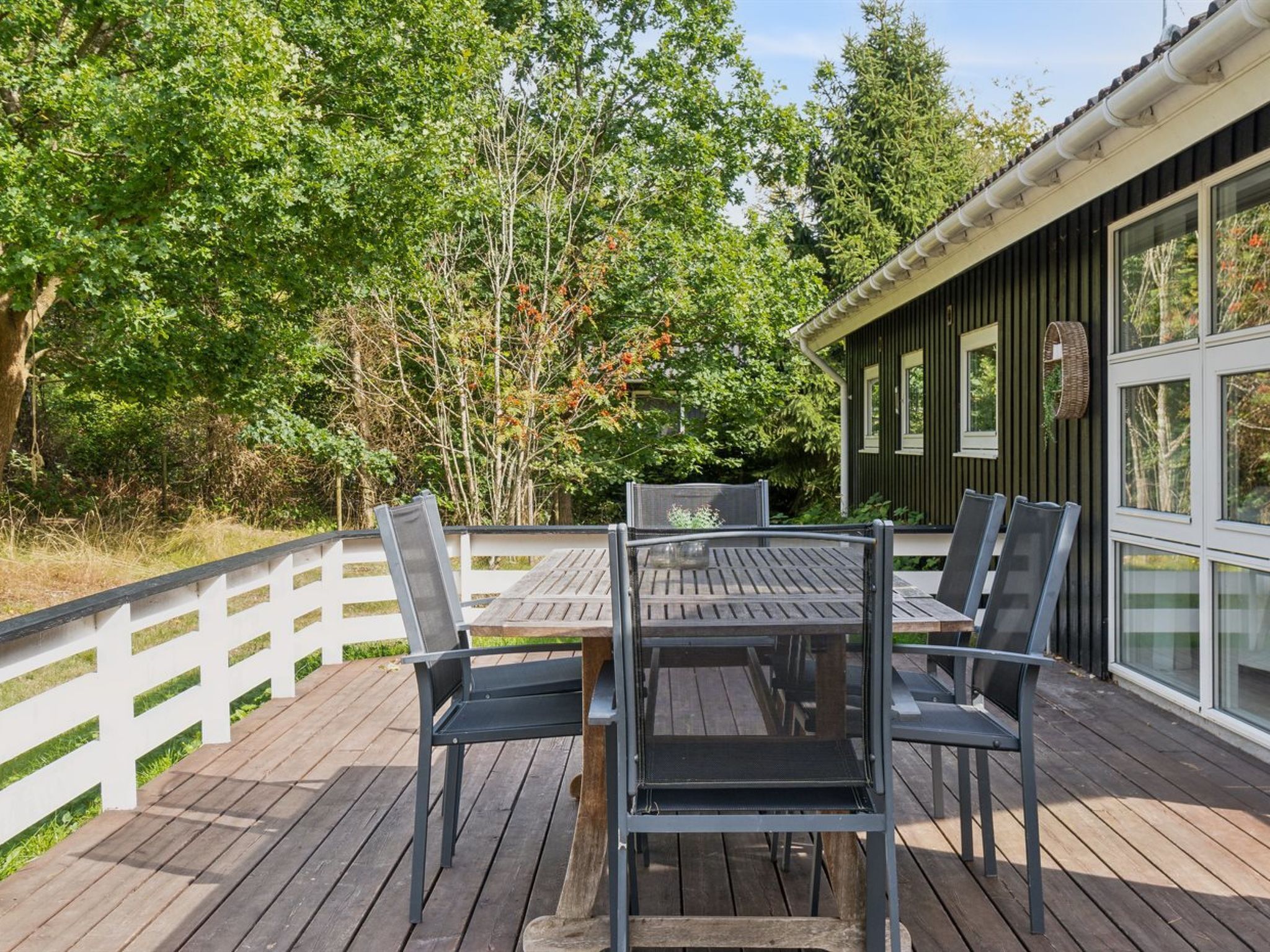 Une terrasse avec une table et des chaises, entourée d’une clôture blanche et d’arbres.