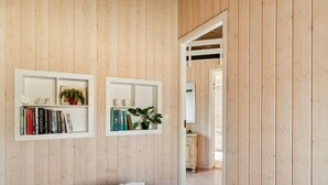 A bedroom with a wooden panel wall, a bed with white bedding, and two white shelves with books and plants. - "Amola" - 1.6km from the sea by Interhome (Højby)