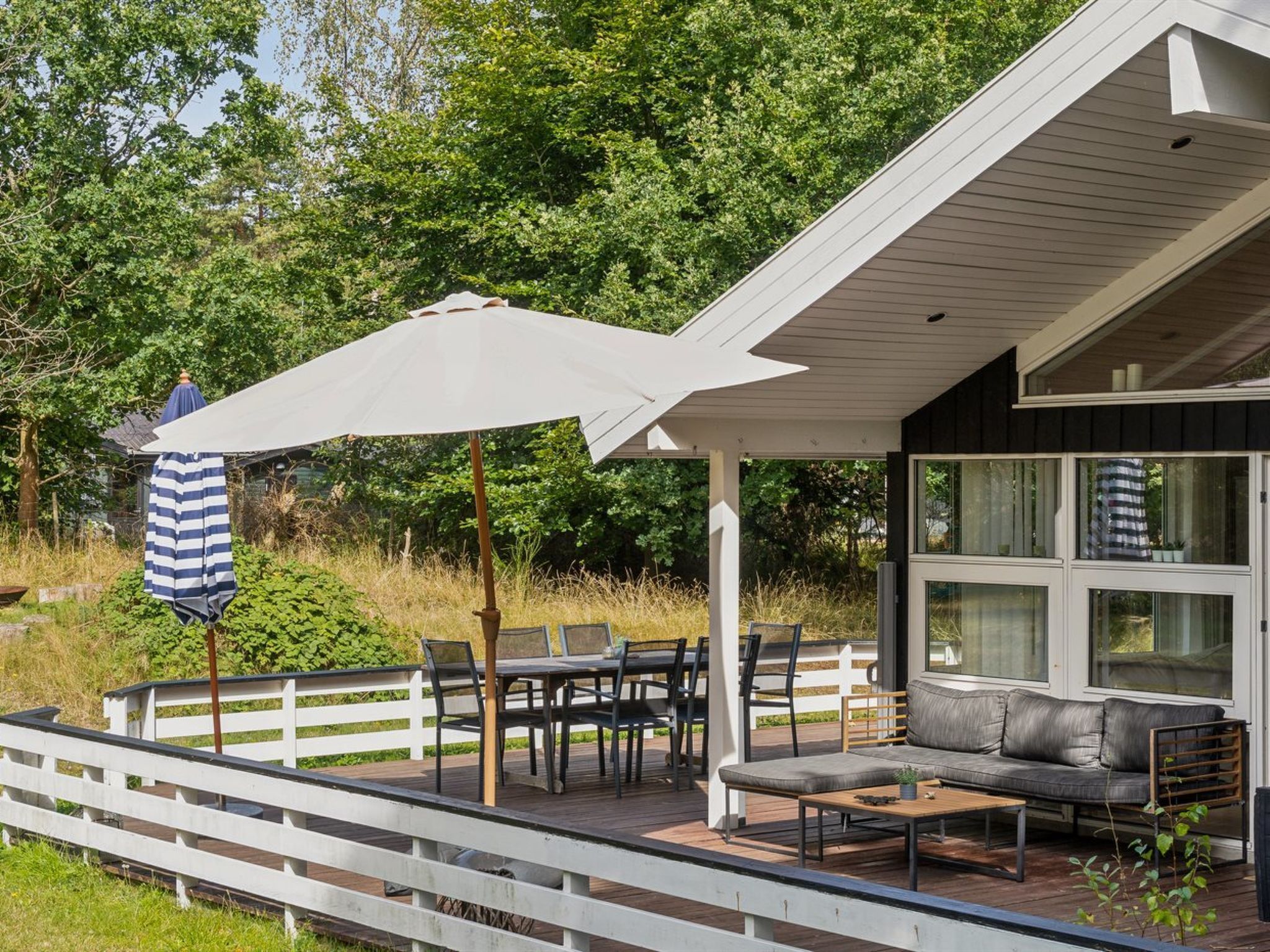 Een overdekt terras met een eettafel en stoelen, een witte parasol en een bank.
