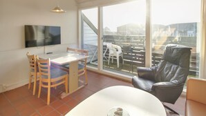 A modern living room with a dining area, large windows, and a TV mounted on the wall.