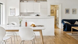 Una cocina moderna con armarios blancos, una isla central y un comedor con sillas blancas.