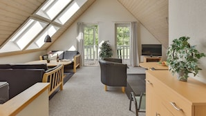 A cozy attic bedroom with a sloped ceiling, skylights, a bed, a desk, and a TV.