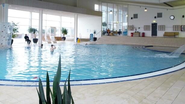 An indoor swimming pool with a water slide, seating areas, and large windows.