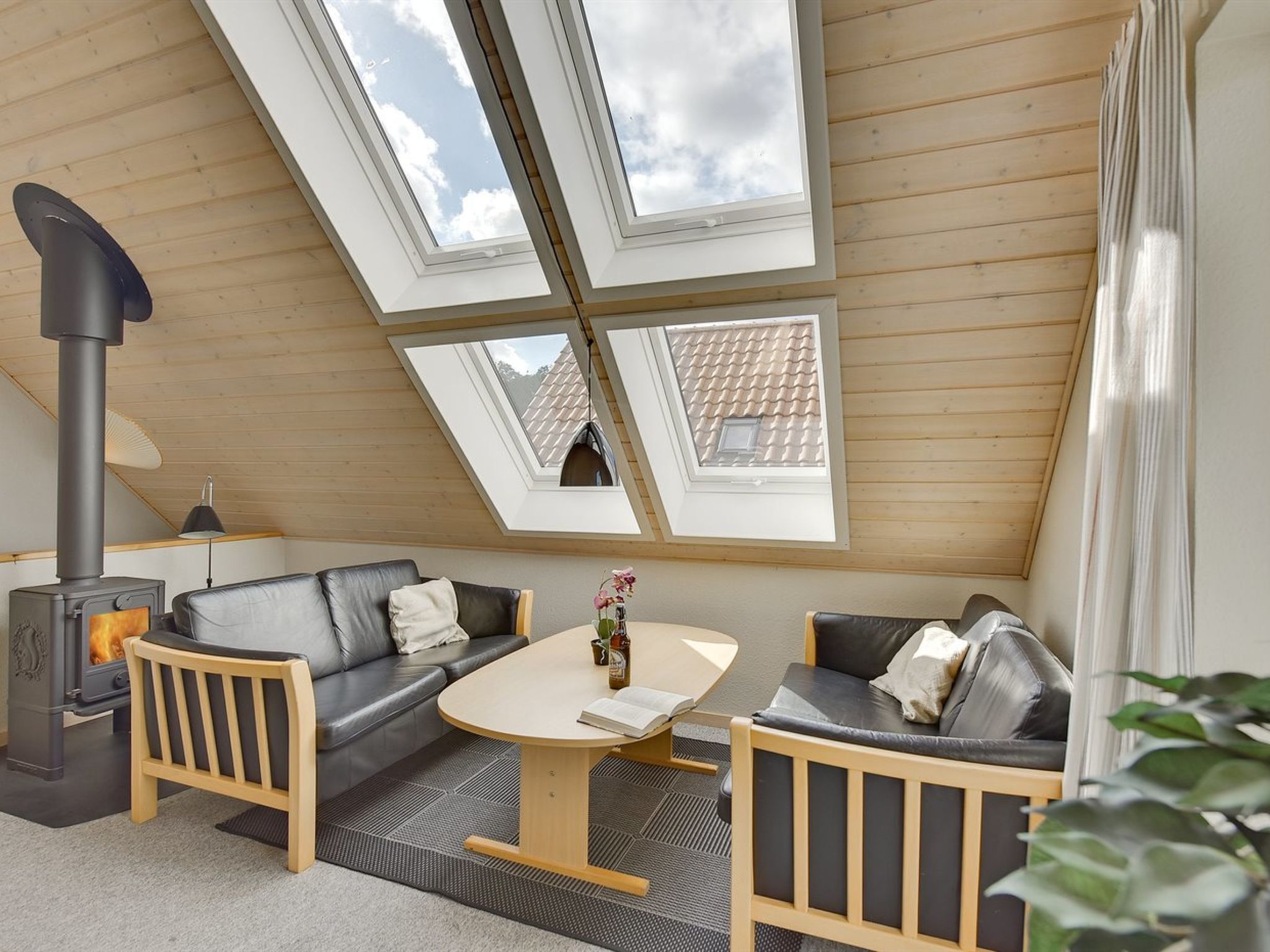 Une pièce chaleureuse au décor moderne de type « loft », comprenant un canapé, une petite table et un poêle à bois encastré.
