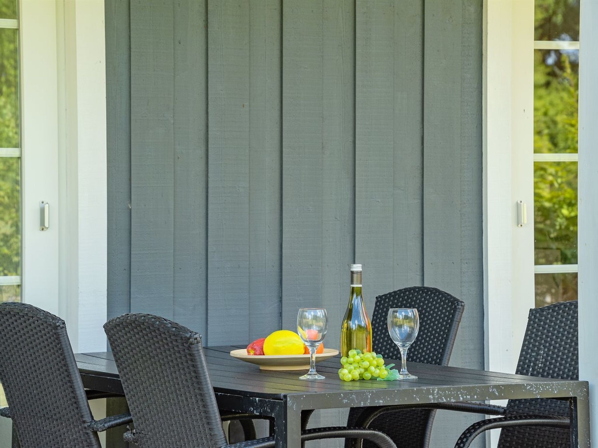 An outdoor dining area with a table set for two, featuring wicker chairs and a wooden table.