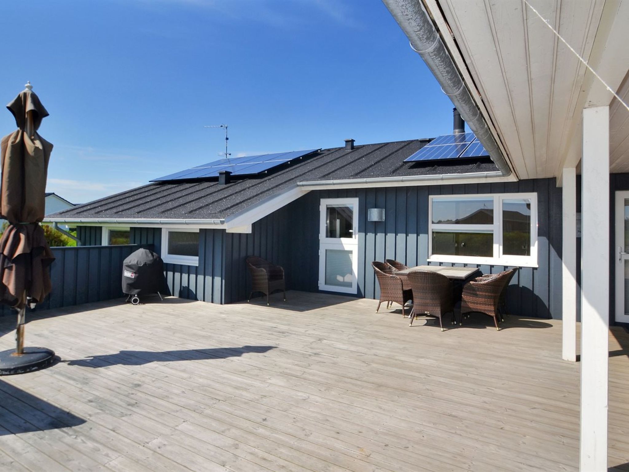 Ett takförsett utomhusområde med ett trädäck, en grill och en sittgrupp med flätade stolar.