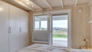 Ein Schlafzimmer mit einem Bett, einem Kleiderschrank und einer Tür zu einem Außenbereich mit Blick auf ein Haus und Vegetation.