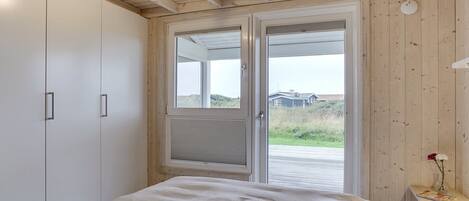 A bedroom with a bed, a wardrobe, and a door leading to an outdoor area with a view of a house and vegetation.