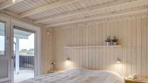 Ein Schlafzimmer mit Holzboden, einem Bett, einem Nachttisch mit Lampe und einem Fenster mit Ausblick.
