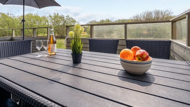 A wooden deck with outdoor furniture, a bottle of wine, and a bowl of fruit. - "Arona" - 1.5km from the sea by Interhome (Fanø)