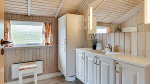 A compact kitchen with wooden walls and ceiling, white cabinets, a bench, and a window with patterned curtains. - "Arona" - 1.5km from the sea by Interhome (Fanø)