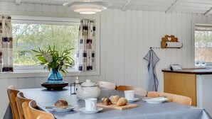A dining area with a table set for four, a vase with flowers, a tea set, and a wooden sideboard with bread. - "Arona" - 1.5km from the sea by Interhome (Fanø)