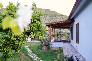 A covered outdoor seating area with a pergola, a stone pathway, and a view of a mountainous landscape. - Nefes Evlerim (Selçuk)