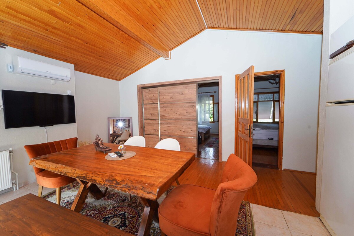 A dining area with a wooden table, orange chairs, a TV mounted on the wall, and a sliding door leading to another room.
