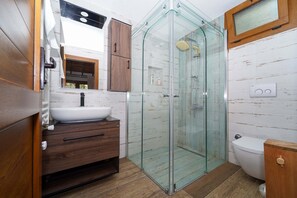 A modern bathroom with a glass shower enclosure, a wooden vanity, and a white sink. - Nefes Evlerim (Selçuk)