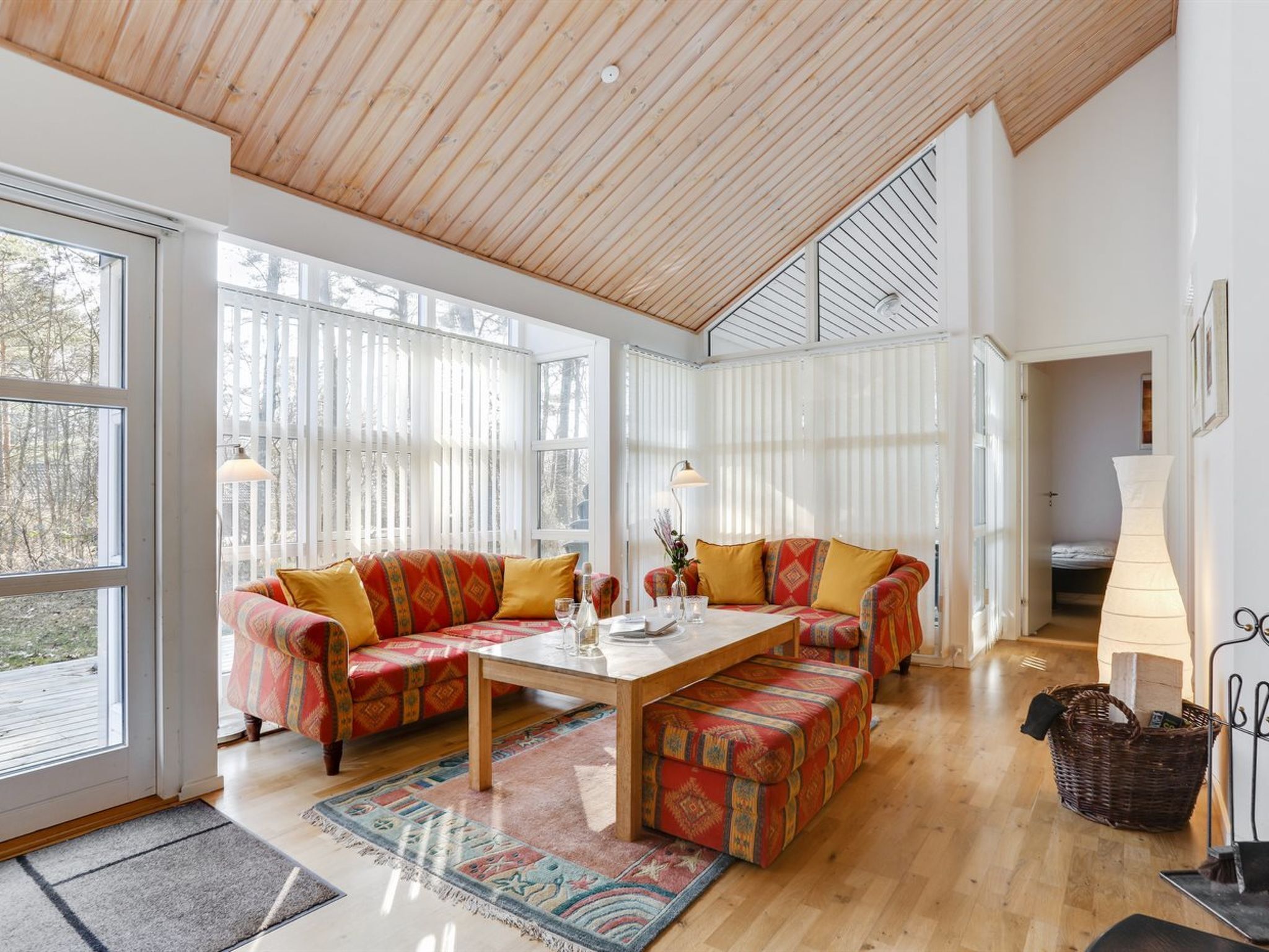 Un vaste salon doté d’un plafond en bois, de grandes fenêtres, d’un ensemble de canapés, d’une table basse et d’un panier en osier.