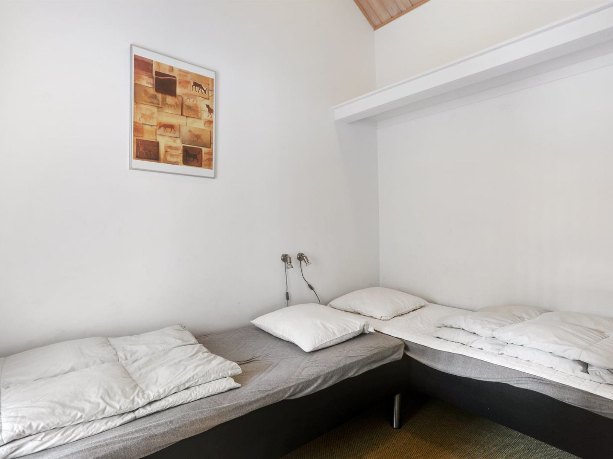 Una habitación pequeña y funcional con dos camas individuales, una pared blanca y un cuadro enmarcado sobre la cama de la izquierda.