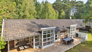 Ett modernt hus med en stor veranda, stora fönster och ett tak täckt med takpannor.