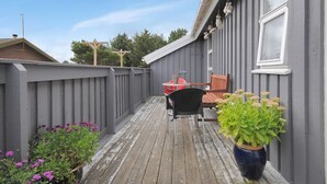 Une terrasse en bois avec une clôture grise, une table avec des chaises et un pot de fleurs.