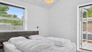 A modern bedroom with a large bed, a wooden headboard, a bedside table, a lamp, and a view of a wooden deck through a sliding door. - "Barth" - 950m from the sea by Interhome (Vig)