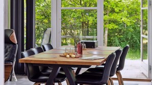 A dining area with a wooden table, black chairs, and a view of lush greenery through large windows. - "Barth" - 950m from the sea by Interhome (Vig)