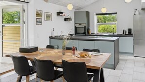 A modern kitchen with a central island, a dining area with a wooden table and black chairs, and a large window providing a view of greenery. - "Barth" - 950m from the sea by Interhome (Vig)
