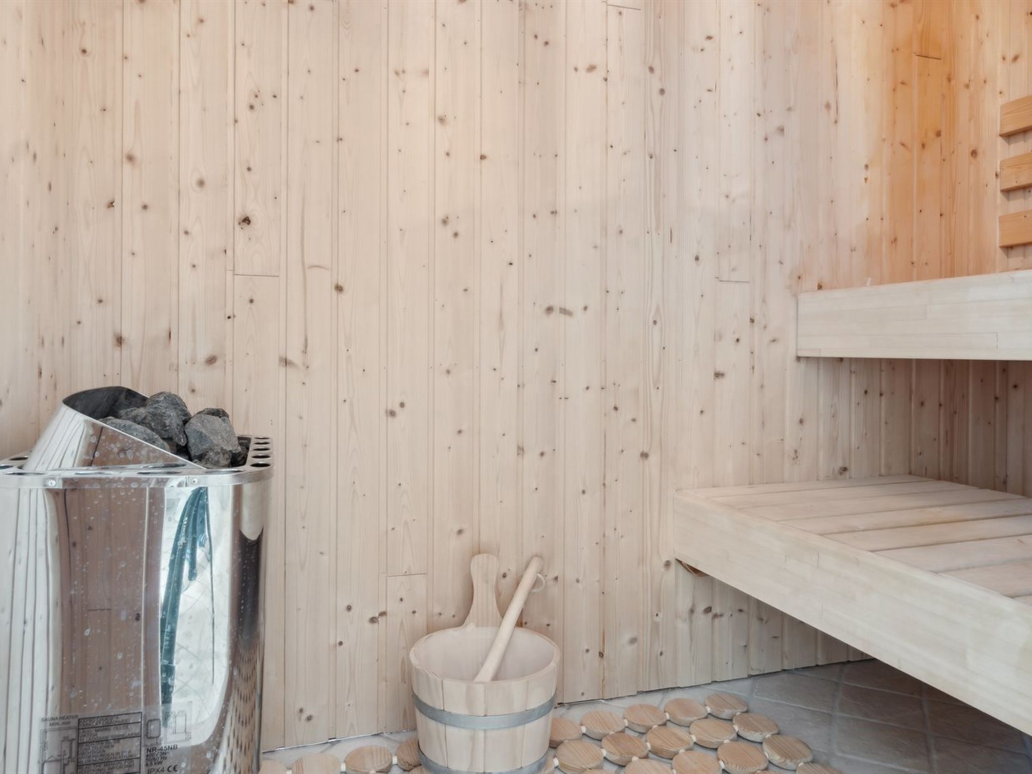 Un sauna avec des murs en bois, un récipient en métal rempli de pierres et un seau en bois avec une louche.