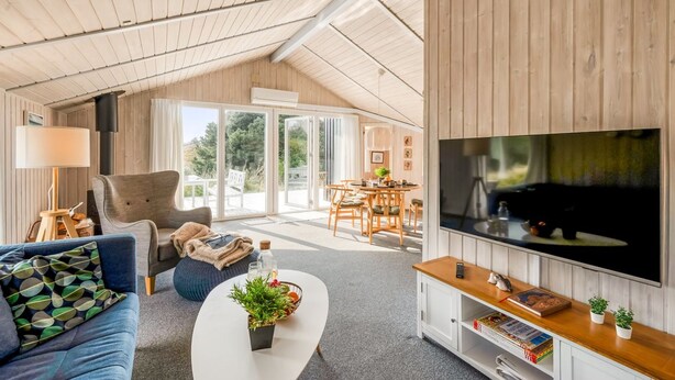 Una sala de estar moderna con un televisor grande, un sofá, una mesa de centro con plantas y una zona de comedor con una mesa y sillas.