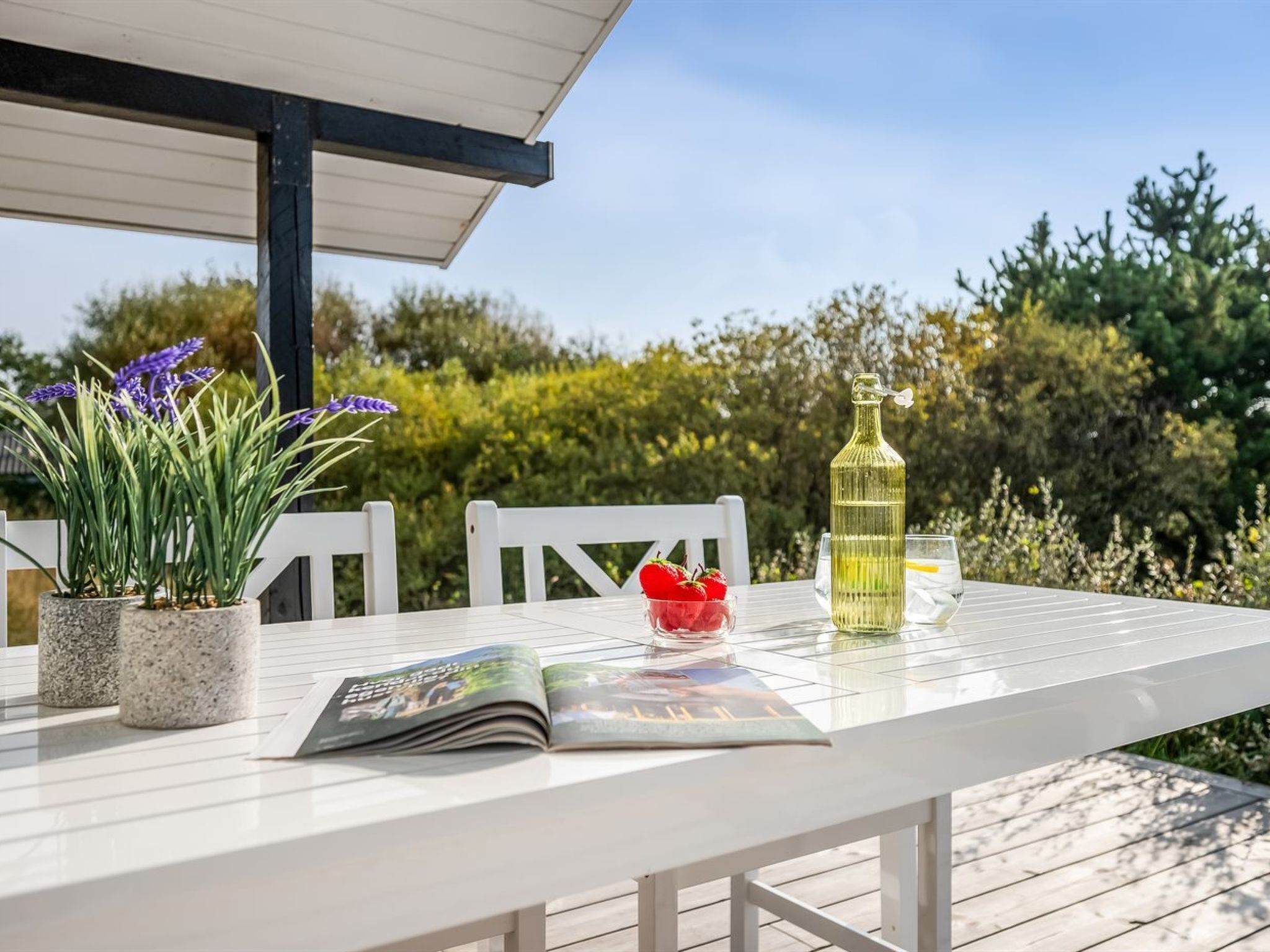 Een witte tafel met een tijdschrift, een fles en een glas.