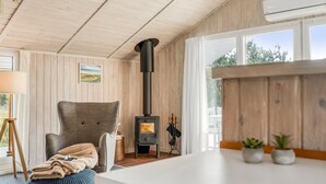 Una habitación acogedora con interior de madera, un ventanal grande, una chimenea, un sillón cómodo y una mesita con plantas.