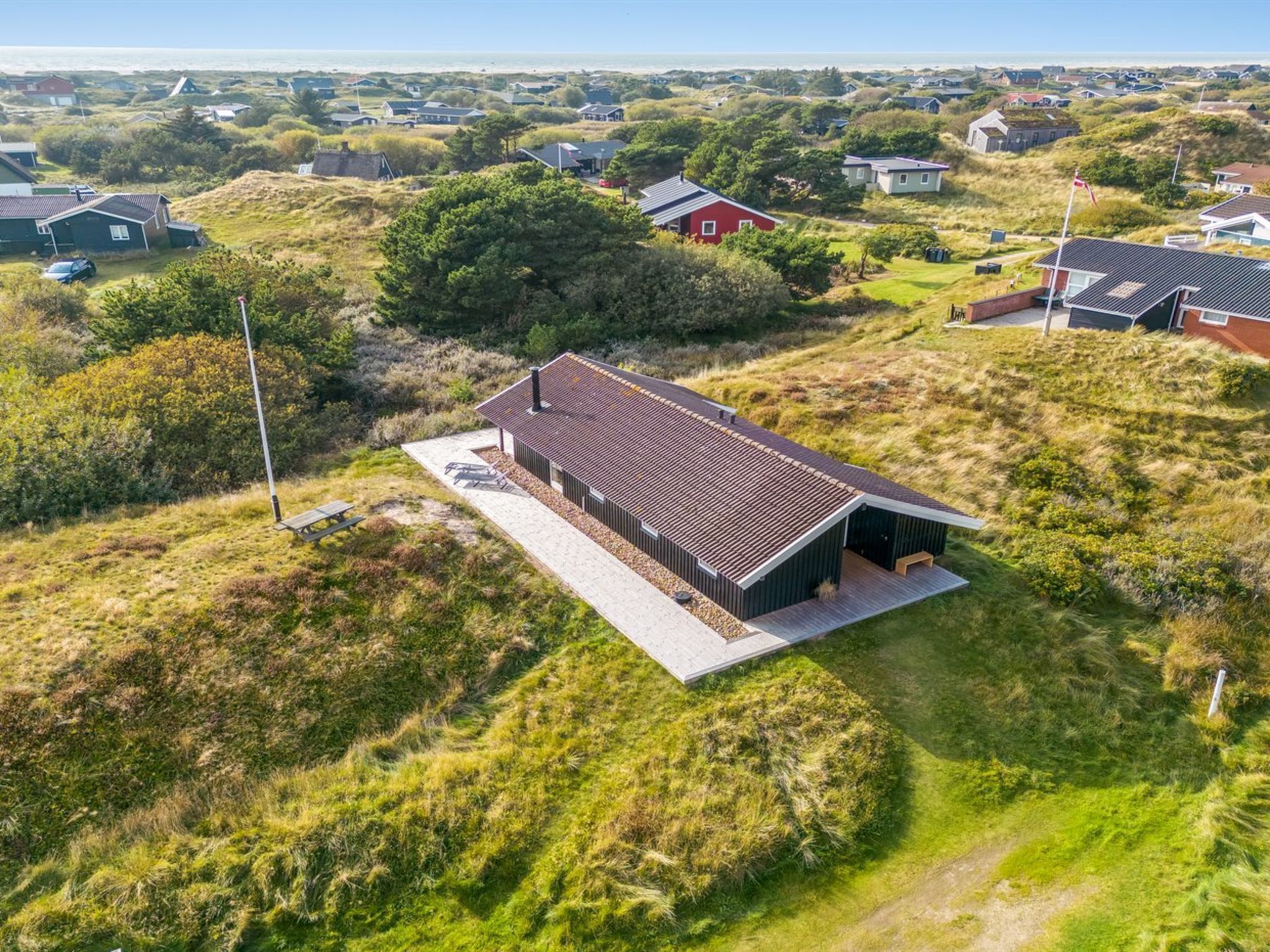 Luchtbeeld van een modern huis met een schuin dak, omringd door grasvelden en andere huizen.