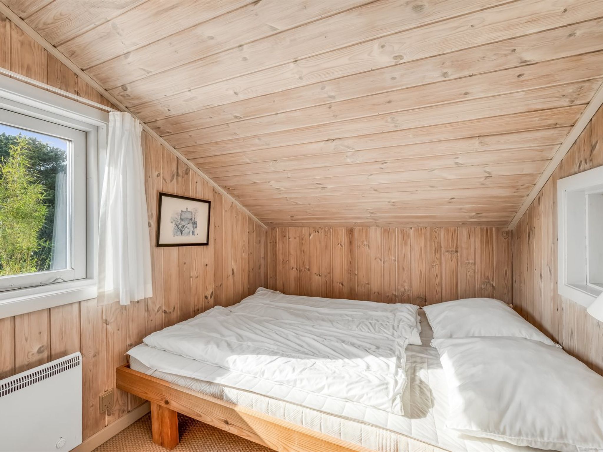 Une petite pièce aux murs lambrissés, avec un lit simple, une fenêtre et un tableau encadré.