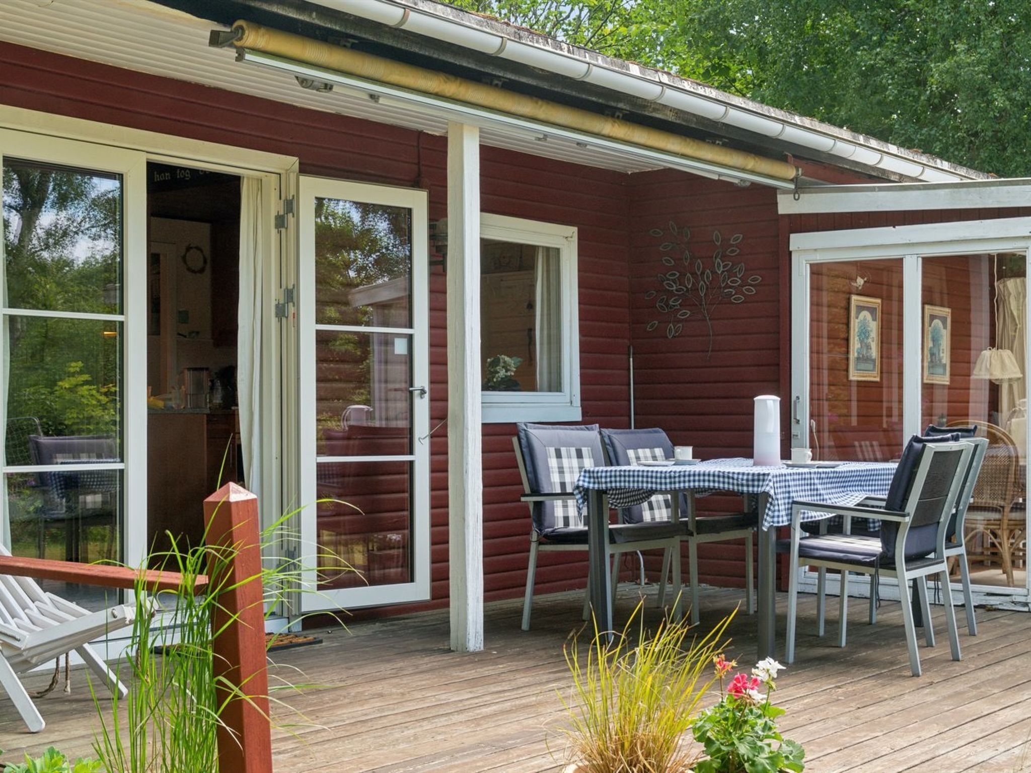 A wooden deck with a table and chairs, a sliding glass door, and a small garden area.