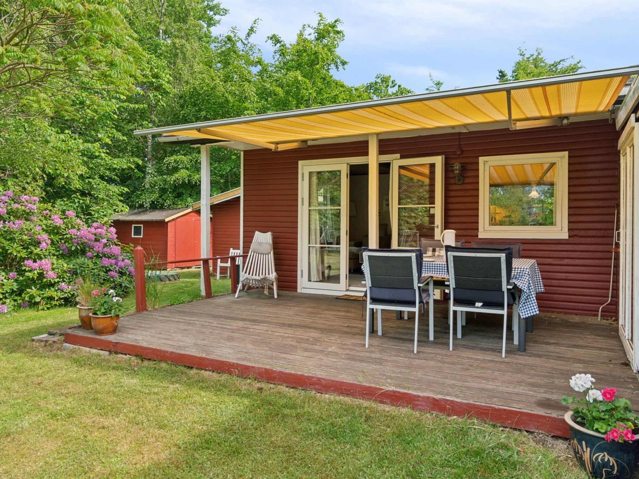 Une terrasse en bois avec des meubles d’extérieur, un patio couvert et un bâtiment rouge doté de portes vitrées.