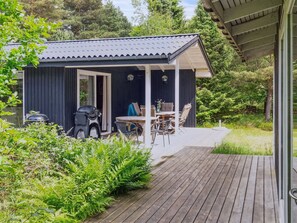 Eine kleine Holzhütte mit Veranda, Grill und Tisch mit Stühlen.