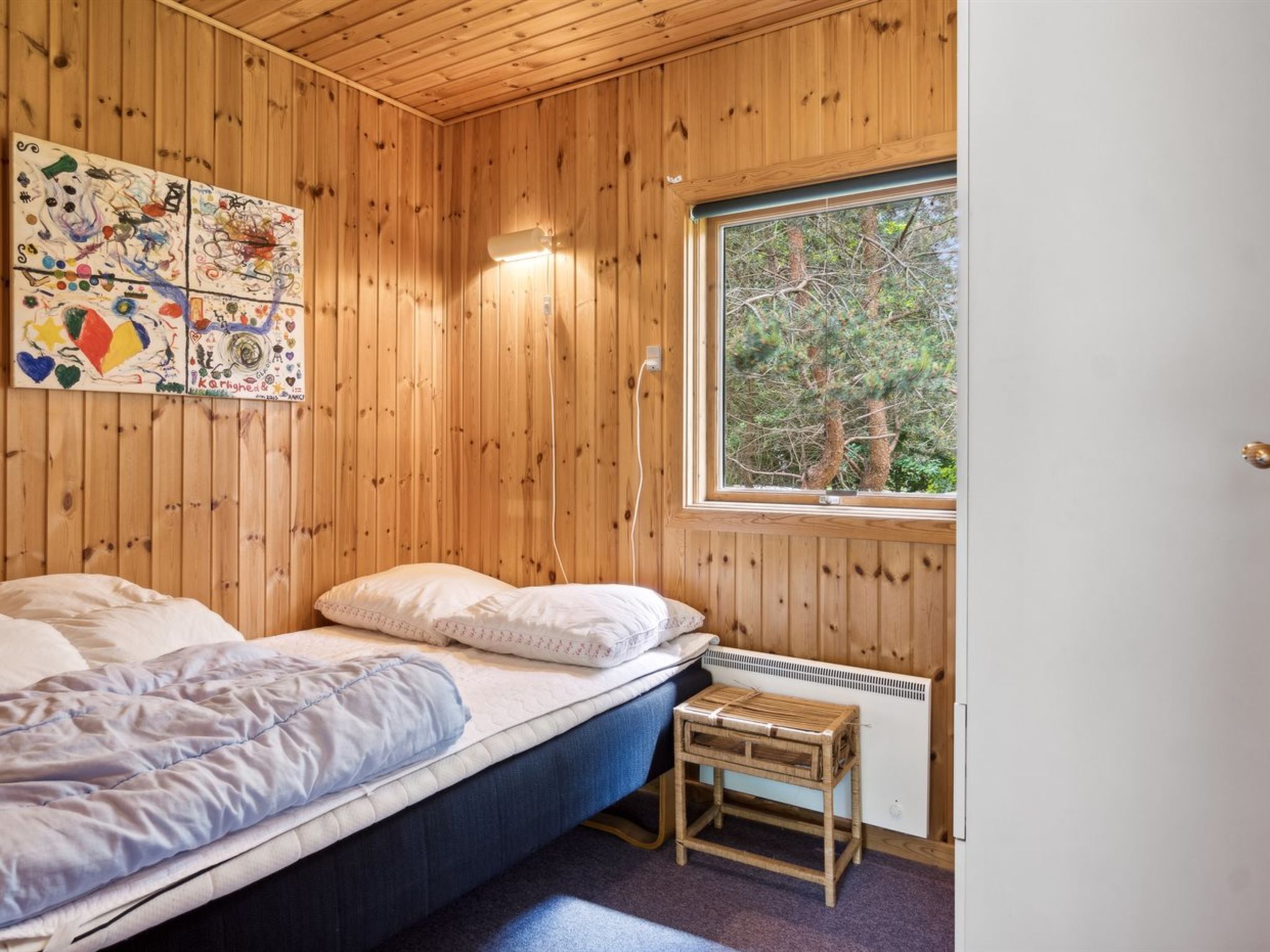 A wooden-paneled room with a bed, a small table, and a window with a view of trees.
