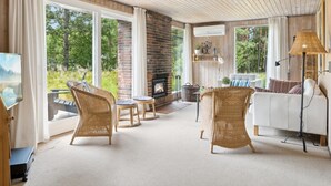 A spacious living room with a fireplace, wicker furniture, a white sofa, and large windows offering a view of the outdoors.
