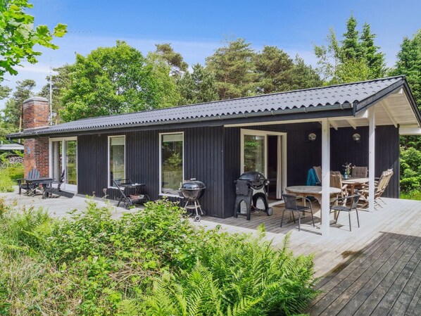 Ein moderner Außenbereich mit einer überdachten Sitzgruppe, einem Grill und einer Holzterrasse.