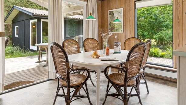 A dining area with a round table, six wicker chairs, and large windows offering a view of the outdoors.